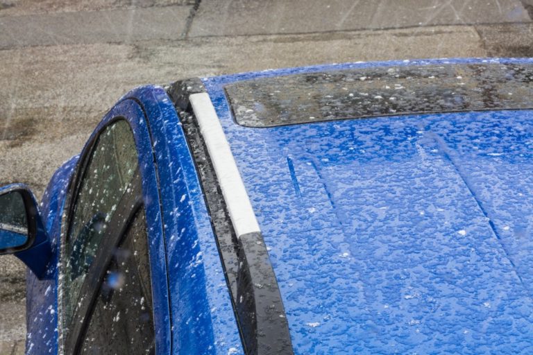 Hail falls on a blue car roof.