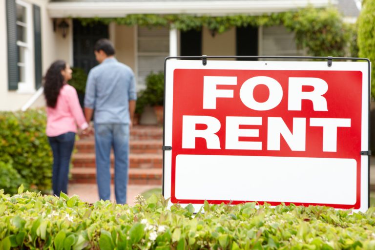 A couple standing outside a house with a red For Rent sign