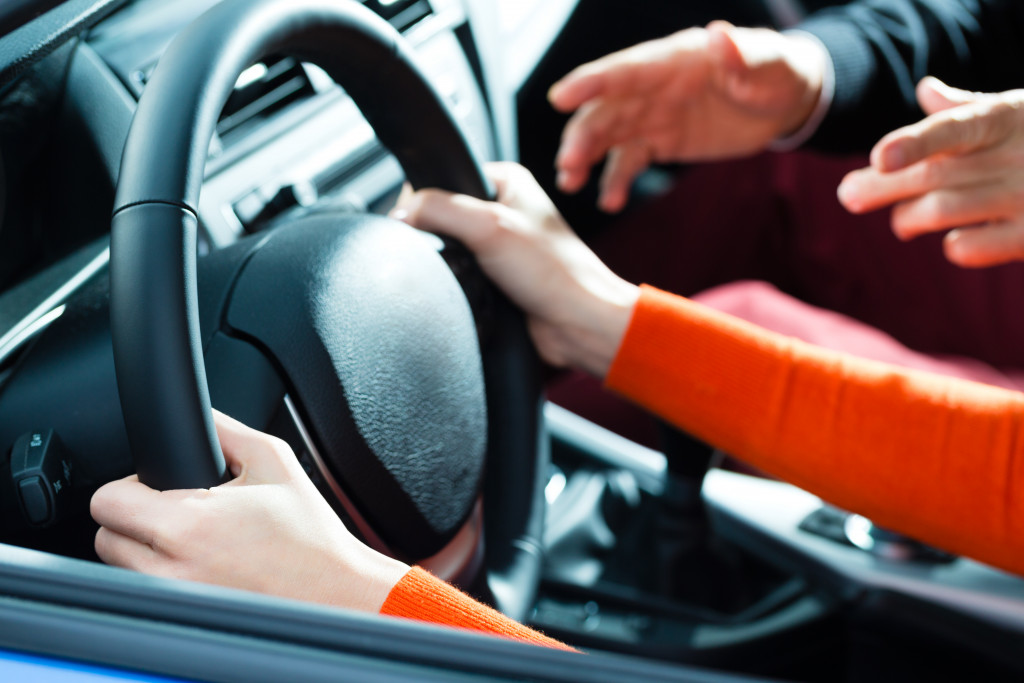 A close-up a woman's hands grasping the steering wheel of a car while an instructor talks to them