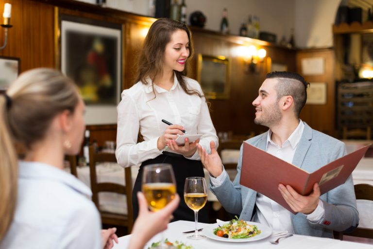 A well-dressed couple gives their order to their waitress in a classic restaurant